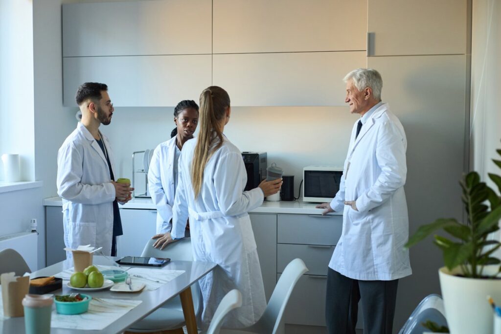 Group of healthcare professionals in lab coats talking in a modern staff workroom, highlighting the role of healthcare furniture in Canada for collaboration and efficiency.