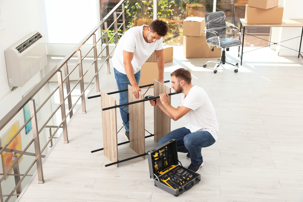 Movers carefully carrying desks and chairs during an office furniture removal project in a commercial office.